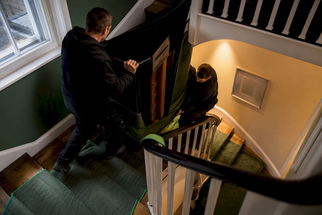 Movers guiding piano around protected stairs